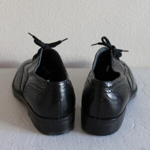 May include: A pair of black leather oxford shoes with brogue detailing. The shoes have laces and a rounded toe.