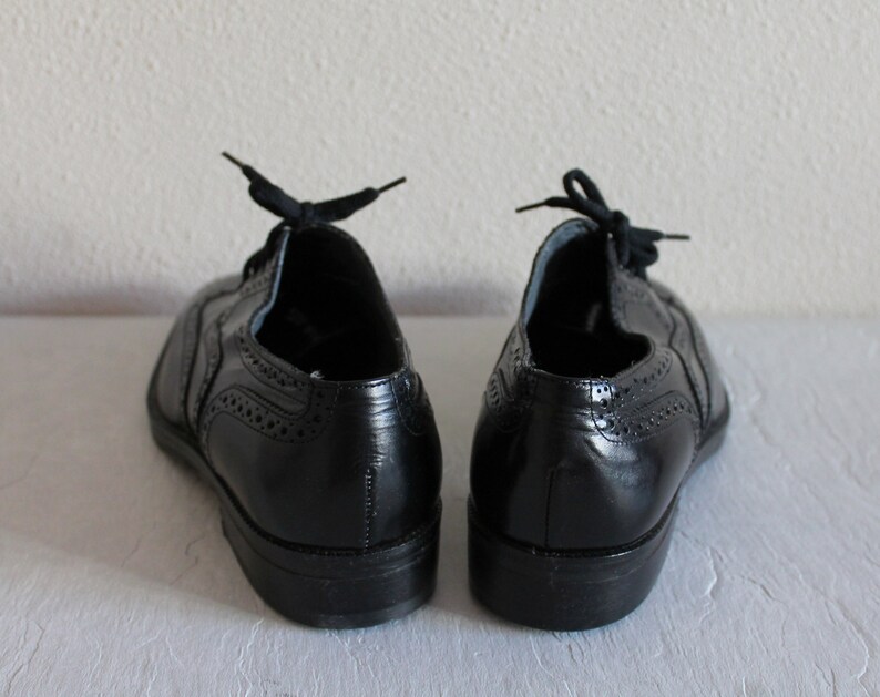 May include: A pair of black leather oxford shoes with brogue detailing. The shoes have laces and a rounded toe.