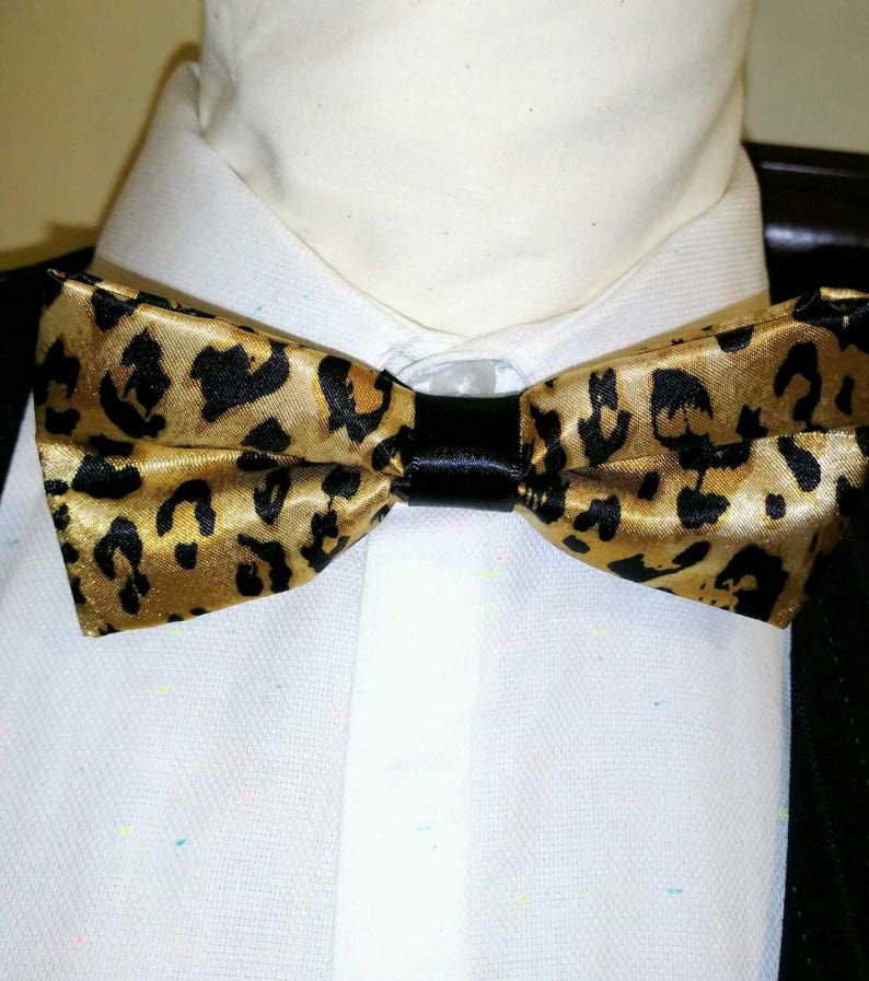May include: A gold and black bow tie with a leopard print pattern.
