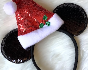 May include: Black sequin Mickey Mouse ears headband with a red sequin Santa hat on top. The hat has a white pom pom and a green holly design.