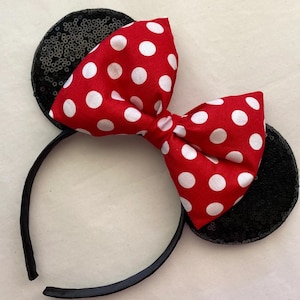 May include: A black headband with two sequined ears and a red bow with white polka dots. The bow is centered on the headband, and the ears are on either side. The headband is a fun accessory.