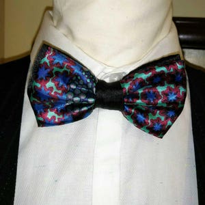 May include: A bow tie with a green, blue, and red patterned design. The bow tie is made of satin and has a black adjustable strap.