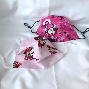 May include: Two pink face masks with a polka dot pattern and a Minnie Mouse design. The masks are made of fabric and have elastic ear loops.