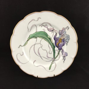 Peut inclure: Une assiette en porcelaine blanche avec un bord dor&eacute; et une fleur violette avec des feuilles vertes peintes dessus.