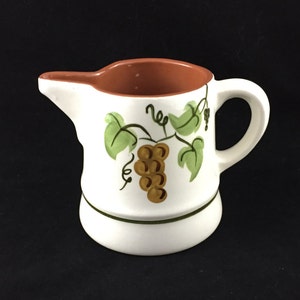 May include: White ceramic pitcher with a brown rim and a painted design of green grape vines and brown grapes.
