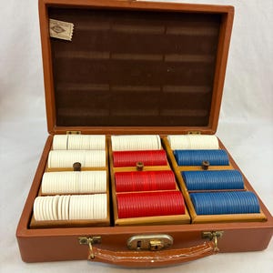 May include: Open brown leatherette poker chip case with a handle and brass hardware. Inside are wooden trays filled with white, red, and blue poker chips. The case is open, revealing a brown felt-lined interior and a small label.