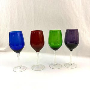 May include: Four colorful wine glasses. Each glass has a different colored bowl: blue, red, green, and purple. The stems are clear with a twisted design, and the bases are round and clear.