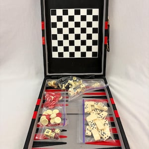 May include: A black game case with gold latches containing a backgammon board with red and black points. Inside are plastic bags holding cream-colored dominoes, red and cream checkers, dice, and chess pieces. A checkerboard is attached to the lid.