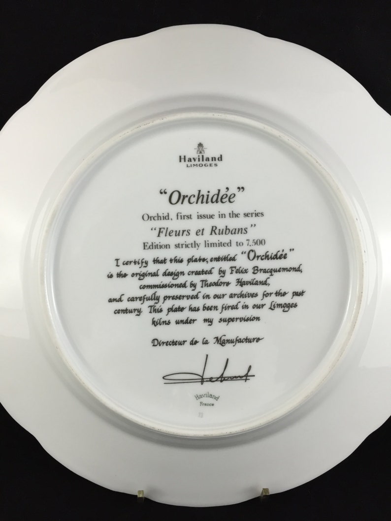 Peut inclure: Une assiette en porcelaine blanche avec une image en noir et blanc d'une orchid&eacute;e. L'assiette fait partie d'une s&eacute;rie en &eacute;dition limit&eacute;e intitul&eacute;e "Orchidee" et "Fleurs et Rubans". L'assiette est sign&eacute;e par le directeur de la manufacture.