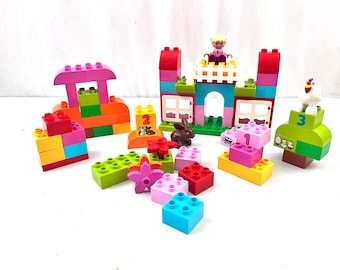 May include: A colorful set of building blocks, including a pink house, a castle, and various other shapes. A small figurine and animal figures are also included. The blocks are in various colors, such as pink, orange, green, and blue.