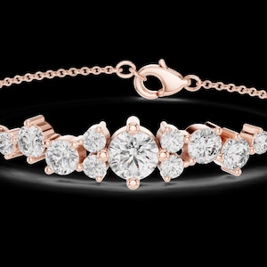 Peut inclure: Un bracelet en chaîne en or rose orné d'un groupe central de pierres rondes, transparentes et facettées. Le design comprend une pierre centrale plus grande entourée de pierres plus petites de tailles variées, avec un fermoir mousqueton.