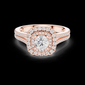 Op de afbeelding: Een roségouden ring met een ronde briljant geslepen middensteen omringd door een dubbele halo van kleine pavé gezette diamanten. De gespleten ringband is ook versierd met rijen kleine diamanten, wat zorgt voor een sprankelend uiterlijk.