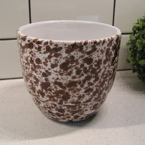 Peut inclure: Un pot en céramique blanche avec des taches brunes. Le pot est rond et a une large ouverture.