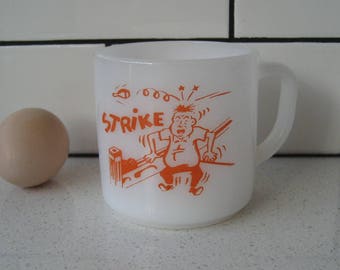 May include: White ceramic mug with an orange cartoon illustration of a person bowling. The mug has the word "STRIKE" printed on it.