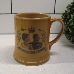 Puede incluir: Una taza de cerámica marrón con un borde plateado y un diseño que conmemora el Jubileo de Plata de la Reina. El diseño presenta un retrato de la reina Isabel II y el príncipe Felipe, con los años 1952 y 1977 impresos en la taza.