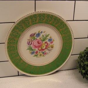 Puede incluir: Un plato de cena de cerámica blanca vintage con un borde verde y dorado. El centro del plato presenta un diseño floral con flores rosas, amarillas y azules.