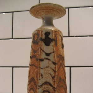 May include: A brown and white ceramic vase with a geometric design. The vase has a wide, flat top and a narrow base.