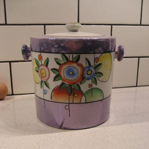 Peut inclure: Un seau à glace en céramique vintage avec un glaçage violet et un motif floral. Le motif présente des fleurs stylisées avec des accents orange, jaune, bleu et vert.