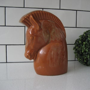 May include: A ceramic horse head sculpture in a brown glaze. The sculpture is a solid piece with a smooth, glossy finish.