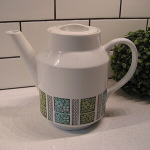 May include: White ceramic teapot with a geometric pattern in black, green, and blue. The teapot has a lid and a handle.