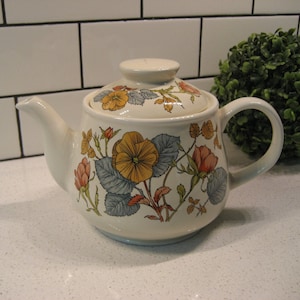 May include: A white ceramic teapot with a floral design featuring yellow, orange, and pink flowers. The teapot has a lid and a handle.