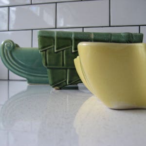 Peut inclure: Trois pots en céramique de formes et de tailles différentes. Le plus grand pot est jaune et a un bord festonné. Le pot du milieu est vert et rectangulaire. Le plus petit pot est vert et incurvé.