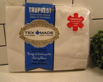 May include: A white Truprest sheet packaged in plastic. The packaging features a blue and gold label with the text "Truprest", "Never Needs Ironing", "Jamais de Repassage", "Tex Made", "Made Right...Here in Canada", "50% Fortrel 50% Cotton", "Tissage de haute qualité", "Luxury Weave", "Un Drap", and "One Sheet". A red flower-shaped sticker with the text "Guaranteed No Iron For Life Free" is on the packaging.