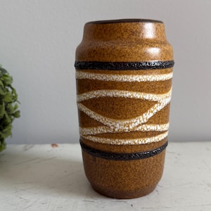 Puede incluir: Un pequeño jarrón de cerámica marrón con diseños geométricos blancos y negros. El jarrón tiene una superficie texturizada.