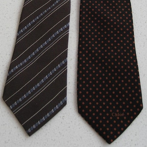 May include: Two brown silk ties. One tie has a white and blue striped pattern. The other tie has a brown polka dot pattern. The polka dot tie has the word "Chloe" printed on it.