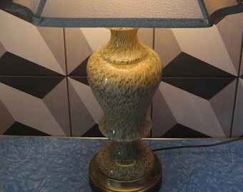 Puede incluir: Una lámpara de mesa con una base de cerámica con estampado marrón y blanco y una pantalla de tela blanca con ribete gris.