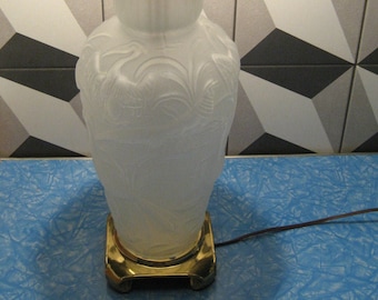 Puede incluir: Una lámpara de mesa de vidrio blanco esmerilado con una base dorada y una pantalla de lámpara con estampado marrón. La lámpara está sobre una superficie azul.