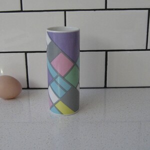 May include: A white ceramic vase with a geometric pattern in shades of purple, pink, blue, yellow, and grey.