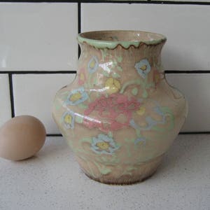 Op de afbeelding: Een keramische vaas met een bloemenpatroon in tinten roze, blauw en groen. De vaas heeft een rond lichaam en een licht uitlopende opening.