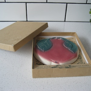 Könnte beinhalten: Eine Keramik-Schale in Apfelform mit grünen Blättern und einem rosafarbenen Zentrum, in einem braunen Karton mit dem Aufdruck "Keep Your Dishes Warm" auf der Schachtel.