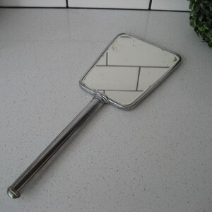 May include: A silver handheld mirror with a rectangular shape and a long handle.