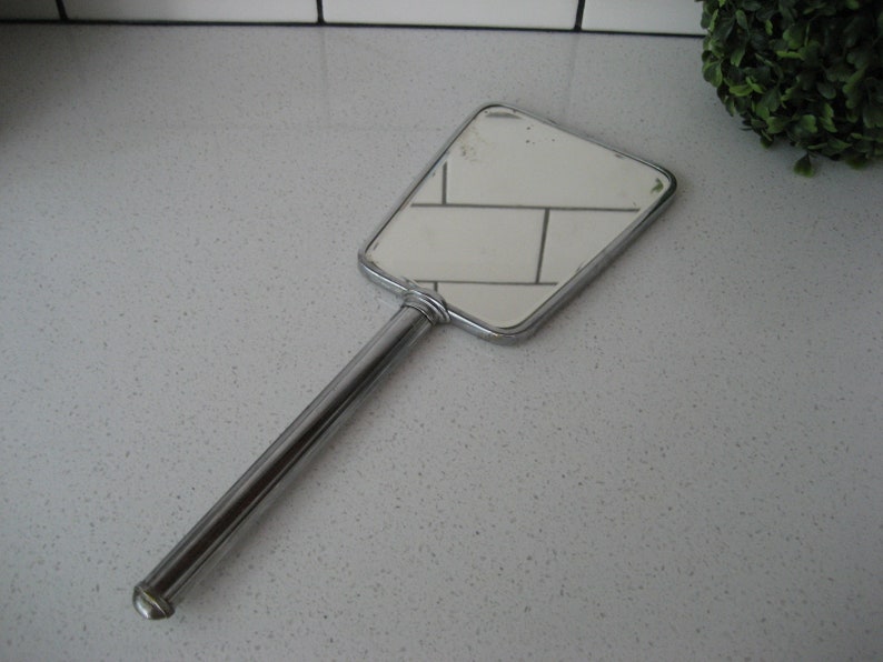 May include: A silver handheld mirror with a rectangular shape and a long handle.