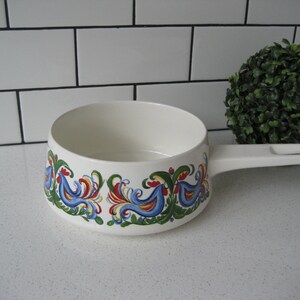 May include: White ceramic saucepan with a blue, red, yellow, and green floral pattern. The saucepan has a white handle.
