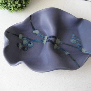 May include: A blue ceramic serving dish with a wavy edge and a design of white and blue branches with blue berries.