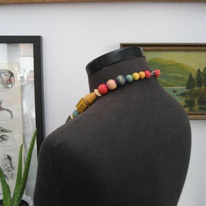 May include: A colorful beaded necklace with red, yellow, blue, and green beads. The necklace is made of wood and is strung on a black cord.
