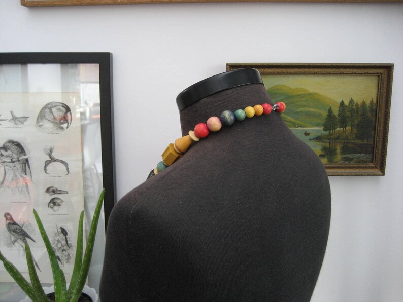 May include: A colorful beaded necklace with red, yellow, blue, and green beads. The necklace is made of wood and is strung on a black cord.
