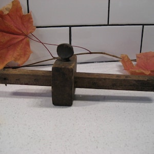 May include: A wooden tool with a metal knob and a ruler on the side. The tool is used for marking and measuring.