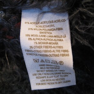 May include: White fabric label with black text listing the material composition of a garment. The label reads: 41% Acrylic, 31% Nylon, 18% Wool, 5% Alpaca, 1% Mohair, 3% Other Fibers. The label also includes care instructions: Hand wash cold, mild detergent, do not wring or twist, use only non-chlorine bleach, reshape and lay flat to dry, low iron as needed, for best results dry clean.