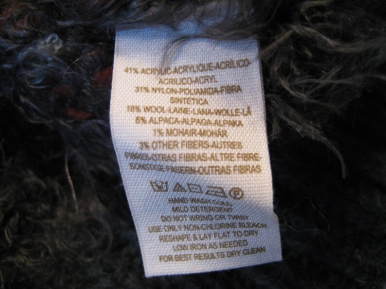 May include: White fabric label with black text listing the material composition of a garment. The label reads: 41% Acrylic, 31% Nylon, 18% Wool, 5% Alpaca, 1% Mohair, 3% Other Fibers. The label also includes care instructions: Hand wash cold, mild detergent, do not wring or twist, use only non-chlorine bleach, reshape and lay flat to dry, low iron as needed, for best results dry clean.