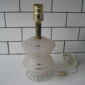 Op de afbeelding: Een vintage roze glazen tafellamp met gouden accenten en een heldere kristallen voet. De lamp heeft een wit snoer en stekker.