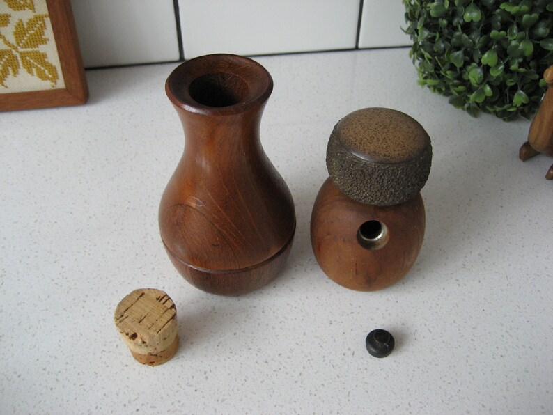 K&ouml;nnte beinhalten: Zwei Flaschenverschl&uuml;sse aus Holz, einer mit runder Oberseite und der andere mit einer vasenartigen Form. Beide Verschl&uuml;sse sind aus dunkelbraunem Holz mit nat&uuml;rlicher Maserung.
