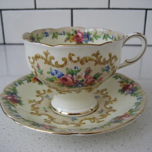Peut inclure: Une tasse à thé et une soucoupe vintage avec un motif floral et doré. La tasse et la soucoupe sont toutes deux blanches avec un motif floral délicat et des accents dorés. La tasse a un bord festonné et une anse.