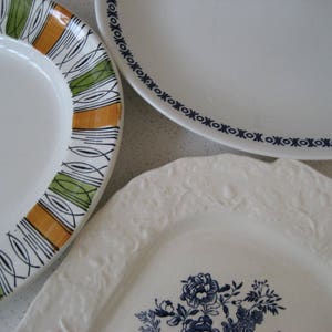 May include: Three ceramic plates with different patterns. The first plate has a white background with orange, green, and black geometric designs. The second plate has a white background with a blue and white geometric design. The third plate has a white background with a blue floral design.