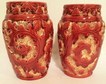 Puede incluir: Dos jarrones de cerámica roja con intrincados diseños florales blancos. Los jarrones tienen una superficie texturizada y una forma redondeada.