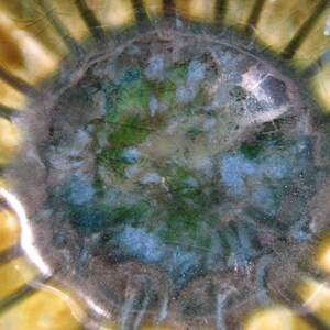 May include: A close-up of a ceramic bowl with a green, blue and brown glaze. The bowl has a scalloped edge and a textured surface.