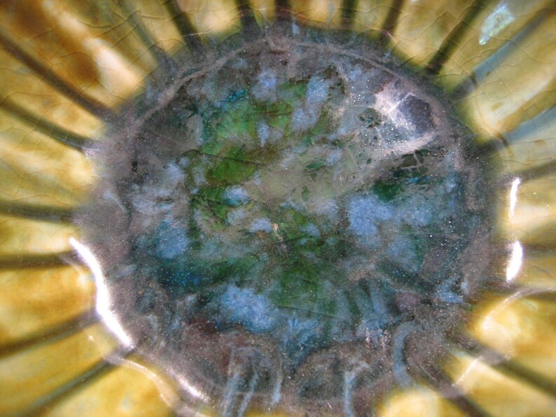 May include: A close-up of a ceramic bowl with a green, blue and brown glaze. The bowl has a scalloped edge and a textured surface.